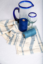 Load image into Gallery viewer, The antique blue, or in French &#39;vieux bleu&#39;, stripes are elegant in any setting.  Here, we&#39;ve highlighted tea towels against the awesome blue of Mexican glass.  Image by Second Star Photography, Whitecourt, Alberta.
